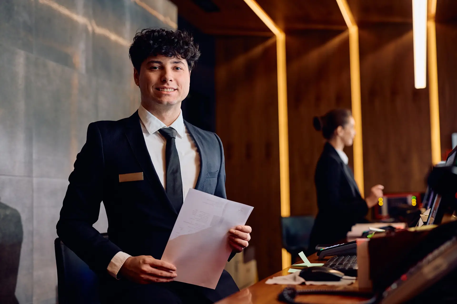 Happy concierge at hotel reception desk looking at camera.