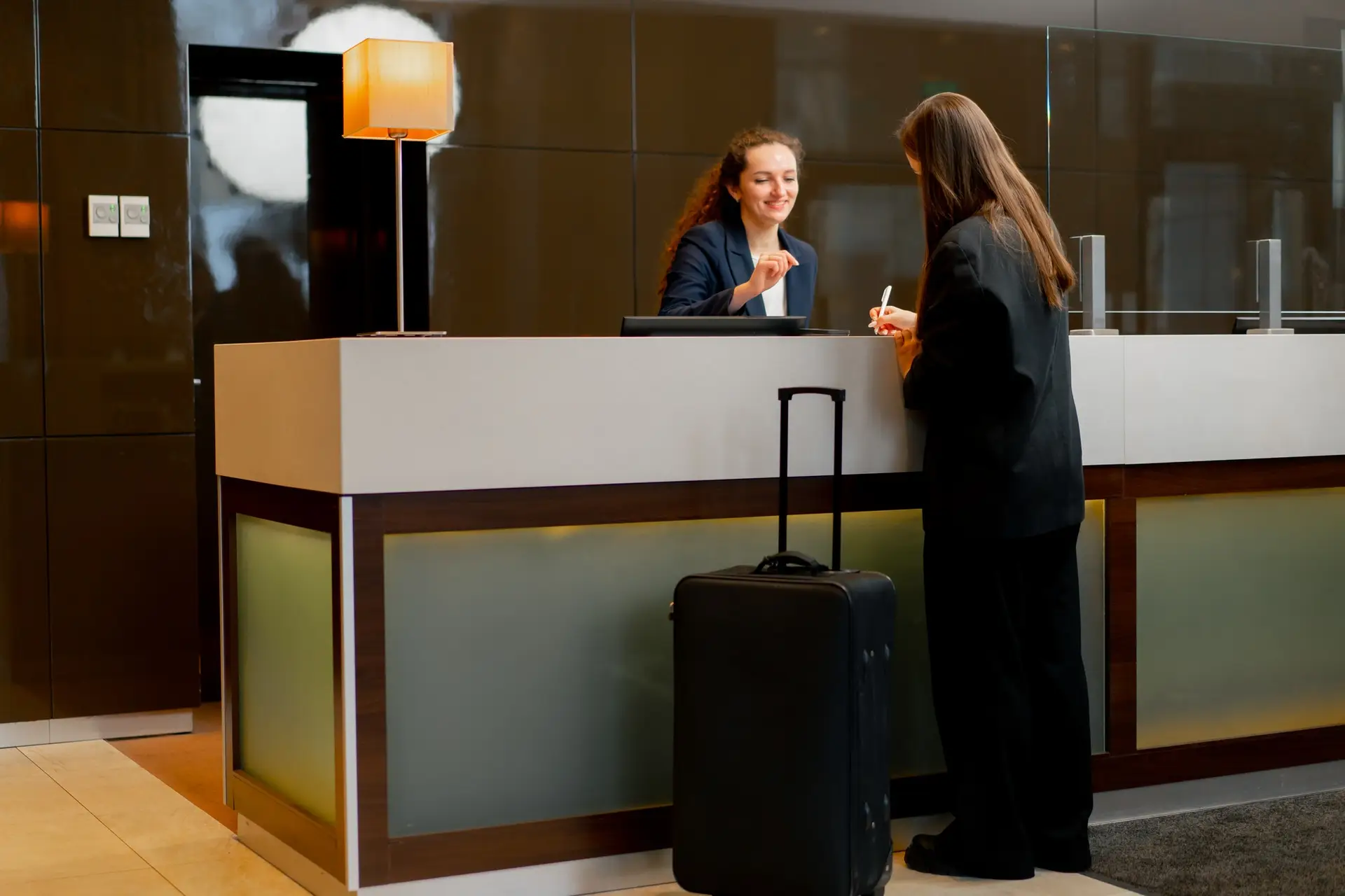 The receptionist at counter meets the guest with luggage in the hotel business travel hospitality